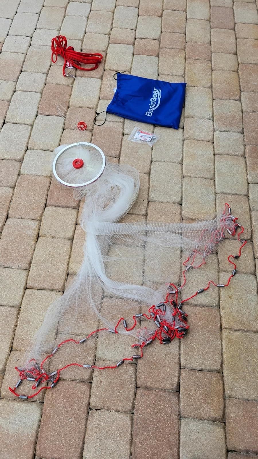 An Easy Throw cast net laid out on patio pavers with its bag and hand ring